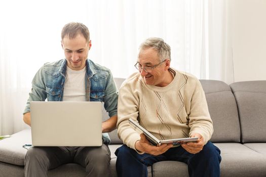 Old father reading album and his son using tablet