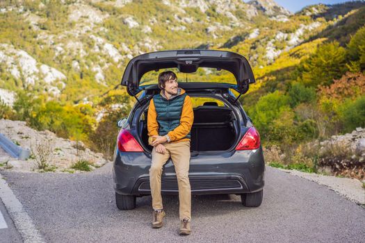 Young man traveler sitting on hatchback car with mountain background in evening time.copy space.