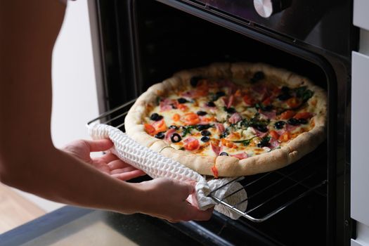 Woman puts pizza pan in oven. Cooking pizza at home concept