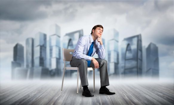 young businessman sits on an office chair, thoughtful and looking up