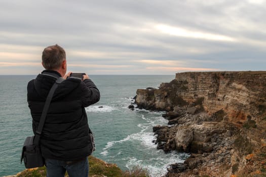 A man make a photo of a beautiful coastline view from the top of a cliff.