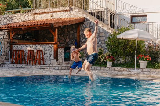 Excited boy in googles jumping in water from shoulders of his father standing in swimming pool