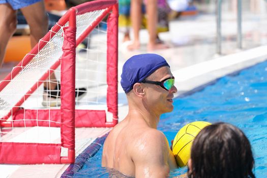 Man at gate in pool plays water polo. Playing water polo in hotel on sunny summer day