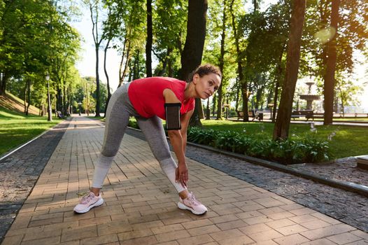 Athletic girl in sport tight clothes doing stretching after the early morning jog. Middle aged active woman, athlete in sportswear exercising outdoor.