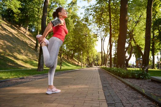 A sportswoman stretches her leg muscles during a morning workout in a city park. Sports and a healthy lifestyle to keep fit. Enjoy sport and keep your body fit