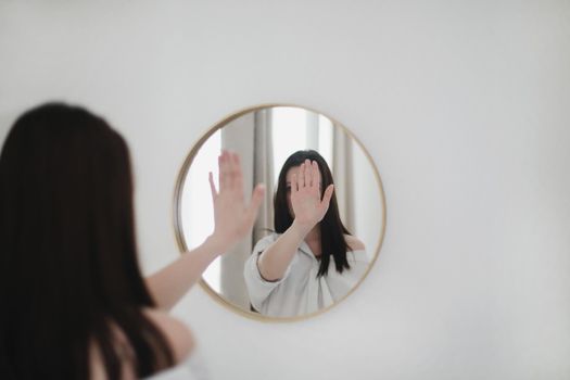 young woman looking in the mirror. Mental health problems in self-isolation at home. Reflection in mirror. Depression, anxiety, phobia, suicide and mental health concept.
