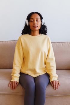 African-American woman sitting on sofa and listening to music in headphones. Concept of mindfulness and affirmative actions. Tranquil relax, calm meditation for personal fulfillment