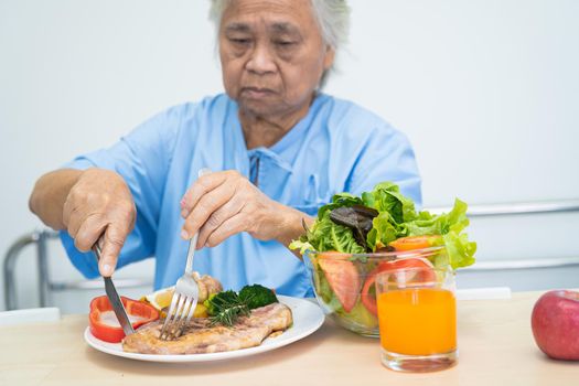 Asian senior or elderly old lady woman patient eating breakfast and vegetable healthy food with hope and happy while sitting and hungry on bed in hospital.