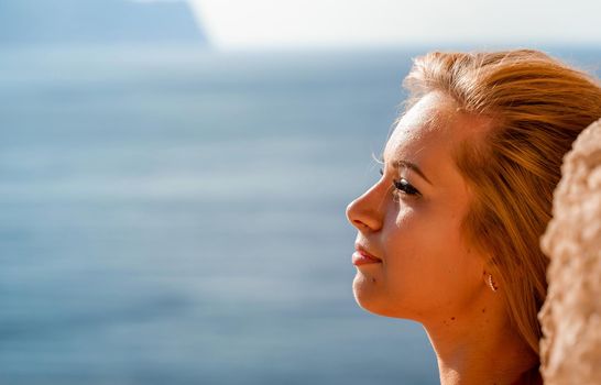 Smiling young woman in a red dress looks at the camera. A beautiful tanned girl enjoys her summer holidays at the sea. Portrait of a stylish carefree woman laughing at the ocean