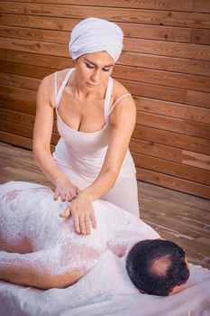 A woman healer performs a ritual with salt, rubs the back of a lying man with salt. Relaxation.