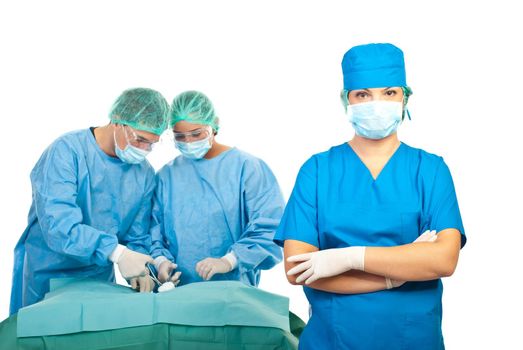 Surgeon woman with mask and protective clothes standing with hands crossed in front of image while her team arrange surgical tools on table and preparing for operation