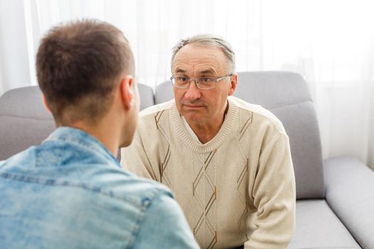 Young man sitting on a sofa smiling and talking with his grandfather