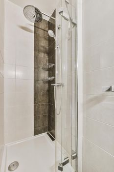 Shower faucets attached to tiled wall near glass partition in washroom at home
