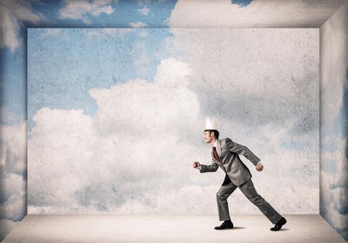 Young handsome businessman wearing white paper crown running in a hurry