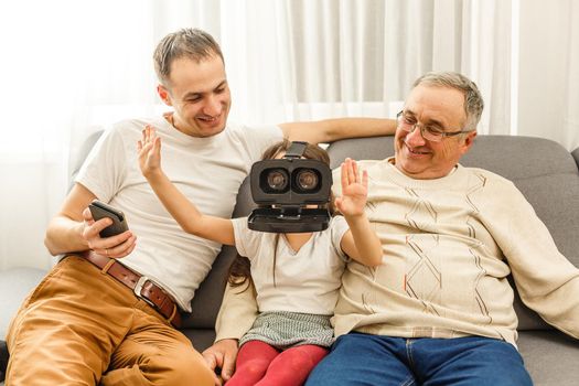 Granddaughter using virtual reality headset with her grandparents in living room at home