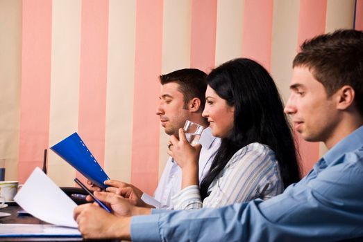 Businesswoman speaking and drinking water in the middle of two men that working and reading papers