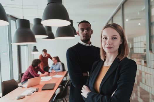 Portrait of happy businesswoman and businessman in modern office. Businessman and businesswoman smiling and looking at camera. Busy diverse team working in the background. Leadership concept. Head shot. High-quality photo