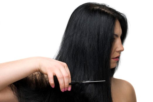 Beautiful brunette woman standing in profile and cutting her long hair with a scissors