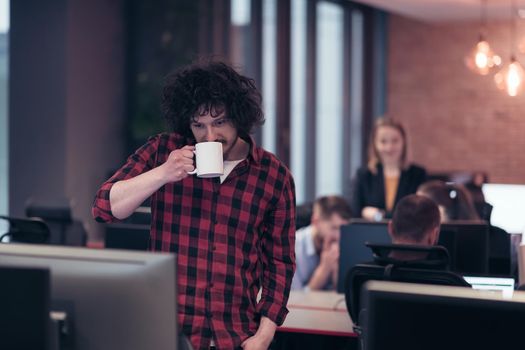 Smiling businessman in afro shirt standing in a modern office with a cup of coffee in hand. Selective focus. High-quality photo