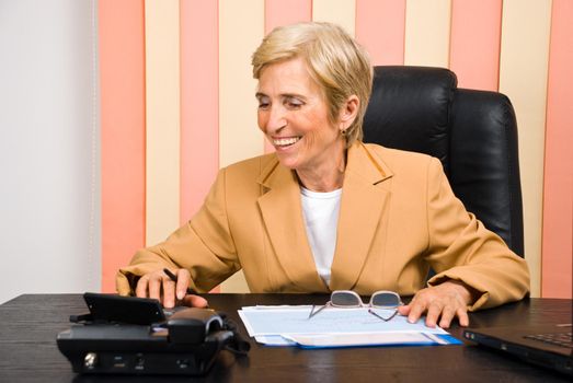 Laughing senior business woman using calculator in office and  having successful calculations