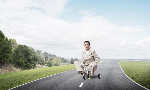 Caucasian woman riding kid's bicycle on asphalt road. Young employee in white business suit biking outdoor. metaphor of ineffective and incompetent work. Beginner level concept with bicyclist.