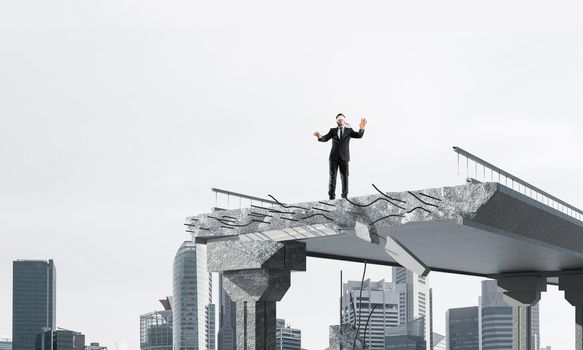 Businessman walking blindfolded on concrete bridge with huge gap as symbol of hidden threats and risks. Cityscape view on background. 3D rendering.