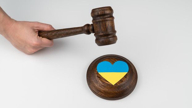 Woman hitting the judge's gavel on the heart with the flag of Ukraine on a white background