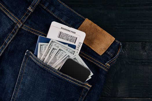 Dollars, smart, passport and plane ticket in your pocket jeans on black wooden background. Top view. Copy space. Still life. Flat lay