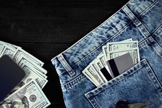 Dollars and cards in your pocket jeans, cash, smart on black wooden background. Top view. Copy space. Still life. Flat lay