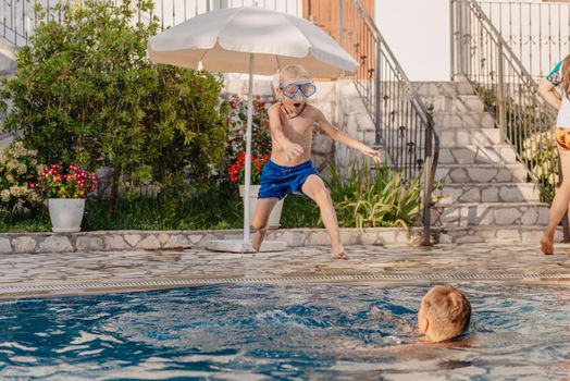 Excited boy in googles jumping in water from shoulders of his father standing in swimming pool