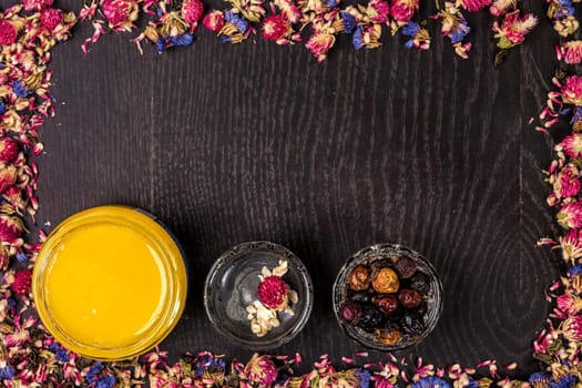 Organic honey in a small jar, mud and clay powder on a wooden background. Frame of dried flowers. Still life. Top view. Copy space