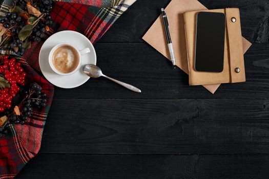 Above view of Smart phone with notebook and cup of latte coffee on black wooden background. Still life. Copy space. Flat lay. Top view