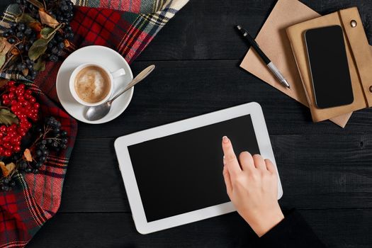 Women hands holding the tablet with black screen above the table with a cup of coffee and smart. Top view, flat lay. Copy space. Still life. Cafe.