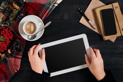 Women hands holding the tablet with black screen above the table with a cup of coffee and smart. Top view, flat lay. Copy space. Still life. Cafe.