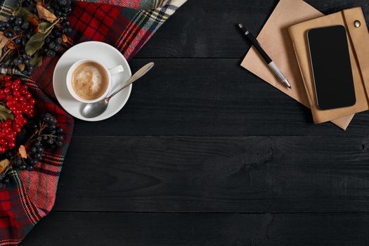 Smartphone with notebook and cup of coffee on wooden background. Top view. Copy space. Still life. Flat lay. Cafe.