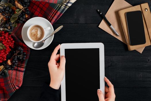 Women hands holding the tablet with black screen above the table with a cup of coffee and smart. Top view, flat lay. Copy space. Still life. Cafe.