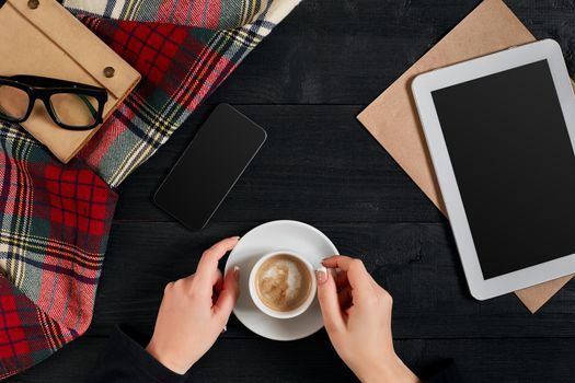 Woman holding cup of coffee and using a digital tablet on a wooden table, technology and communication concept, flat lay. Top view. Still life