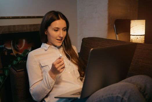 Remote work. A caucasian woman with headphones working remotely on her laptop. A happy businesswoman watching a webinar sitting on the sofa.