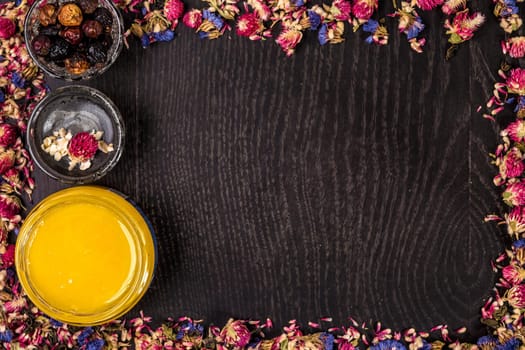 Organic honey in a small jar, mud and clay powder on a wooden background. Frame of dried flowers. Still life. Top view. Copy space