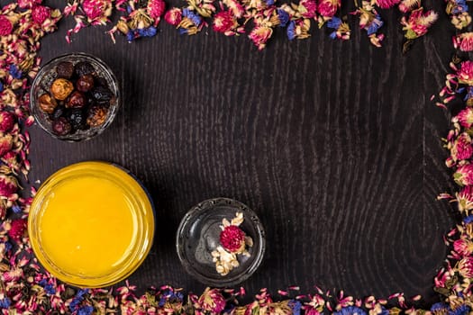 Organic honey in a small jar, mud and clay powder on a wooden background. Frame of dried flowers. Still life. Top view. Copy space