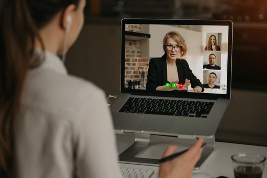 Back view of a woman at home talking with her boss and other colleagues in a video call on a laptop. Businesswoman talks with coworkers on a webcam conference. Business team having an online meeting.