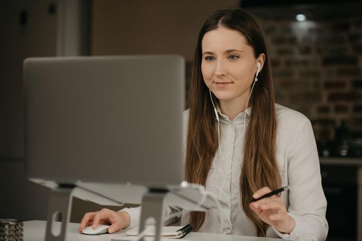 Remote work. A caucasian brunette woman with headphones working remotely on her laptop. A businesswoman in a white shirt doing business at her home workplace.