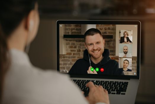 Back view of a woman talking with a business partner and colleagues in a video call on a laptop. Man talks with coworkers on a webcam conference. Multiethnic business team having an online meeting.