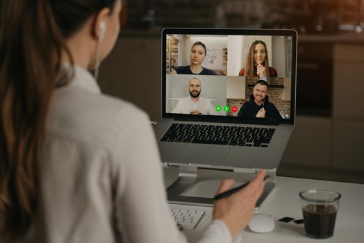 A Back view of a woman working remotely in a video conference with her colleagues during an online meeting. Partners in a video call. Multiethnic business team having a discussion in an online meeting