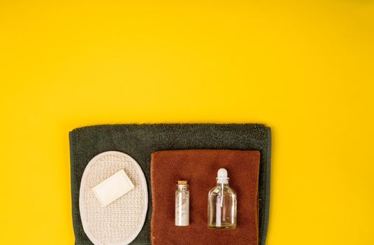 Spa or wellness setting in white colors. Bottles with essential aroma oil, towels, soap on yellow background. Place for text. Top view.