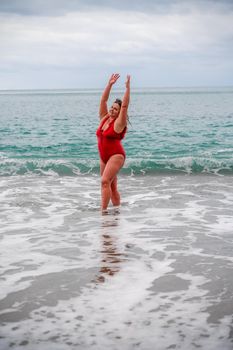 Woman in a bathing suit at the sea. A fat young woman in a red swimsuit enters the water during the surf.