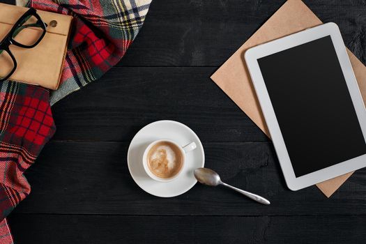 Empty tablet, a cup of coffee, notebook on the desk. Tablet, cup hot coffee on old vintage wooden board. Top view, flat lay. Copy space. Still life. Cafe.