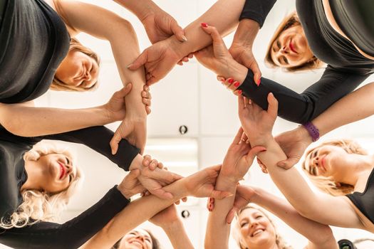 Team of people holding hands. Group of happy young women holding hands. Bottom view, low angle shot of human hands. Friendship and unity concept.