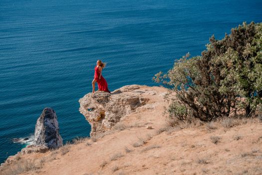 A woman in a red flying dress fluttering in the wind, against the backdrop of the sea