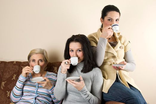Three women friends enjoying a coffee and a conversation in living room,sitting all on sofa